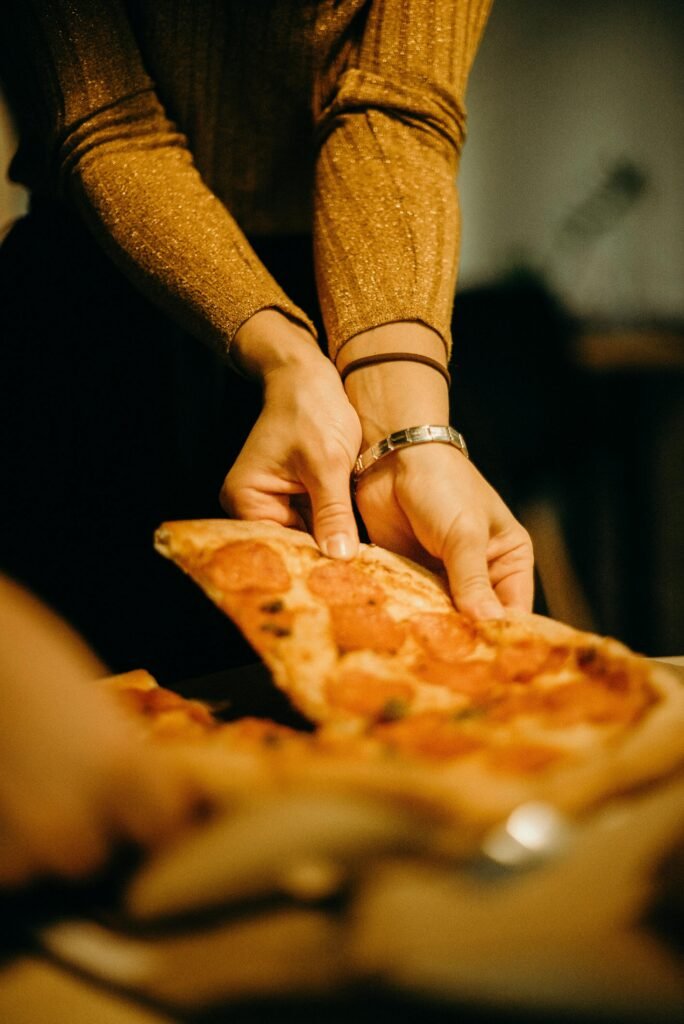 pexels-photo-3171766-3171766 Close-up of hands serving a pepperoni pizza slice indoors, warm and inviting.