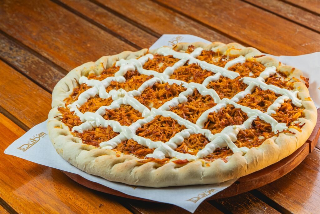 pexels-photo-33458049-33458049 Savory barbecue chicken pizza topped with creamy sauce on a rustic wooden table.